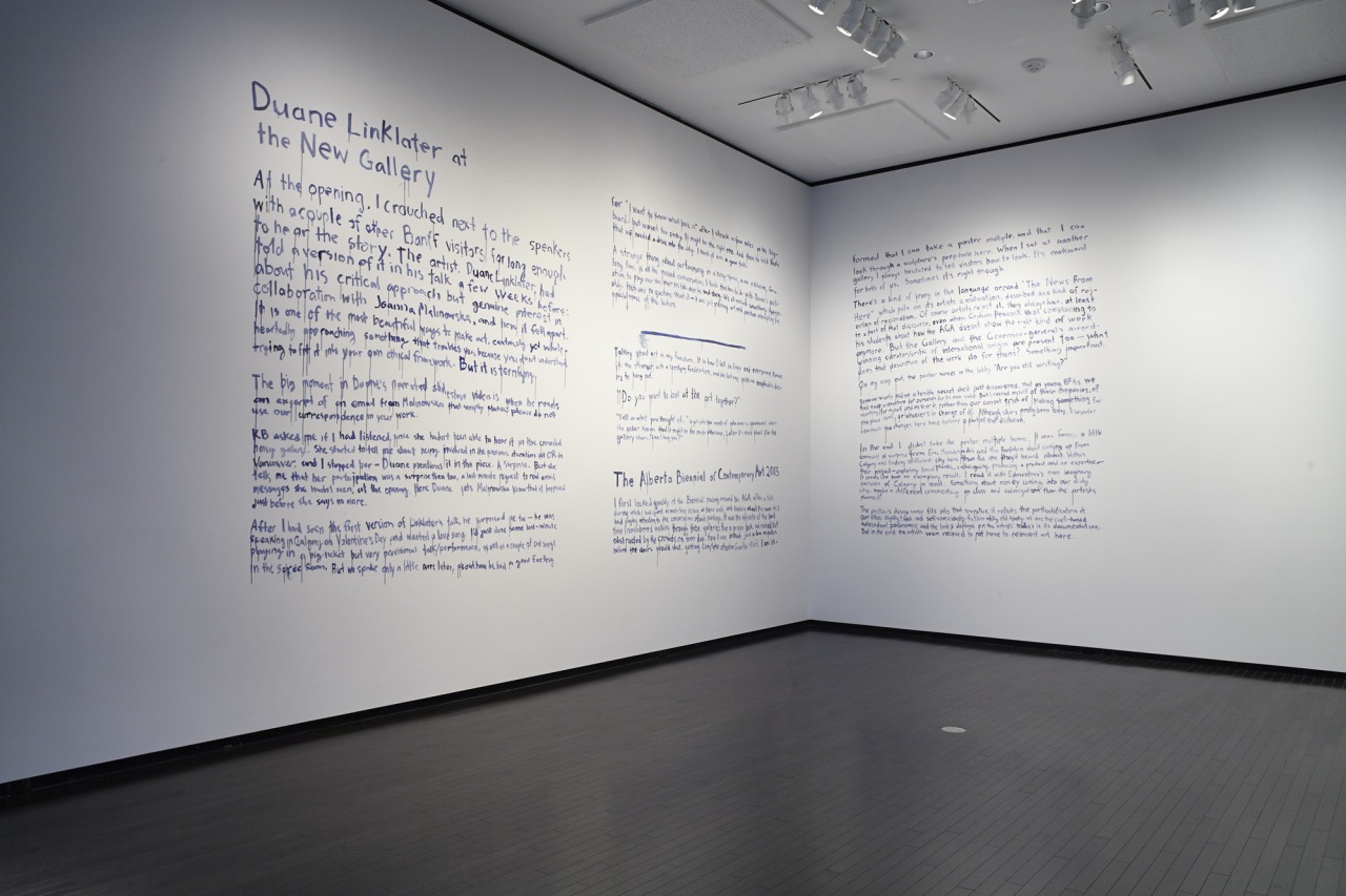 Reviews of Duane Linklater at The New
	Gallery and The Alberta Biennial of Contemporary Art 2013 written in blue paint on
	the wall of the gallery